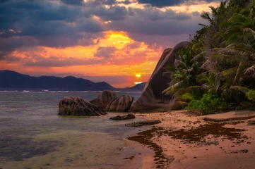 Photo sur Plexiglas Anse Source D'Agent, île de La Digue, Seychelles Colorful sunset over Anse Source D'argent beach at the La Digue Island, Seychelles, with calm water of the Indian Ocean, amazing granite rock formations and mountains in the background.