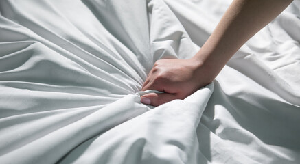Woman hand squeezing white bed sheet during orgasm.