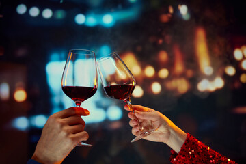 Anniversary celebration and meeting on a date. Male and female hands clinking glasses with red wine over restaurant background. Concept of holidays, celebration, events, relationship