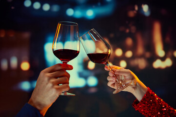 Anniversary celebration, Valentines day date. Male and female hands clinking glasses with red wine over restaurant background. Concept of holidays, celebration, events, relationship