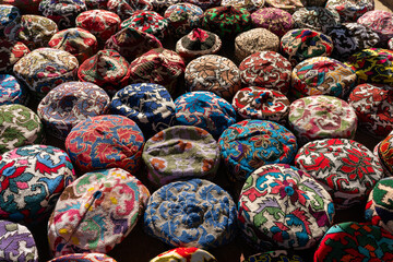 lot of colorful beautiful skullcaps on a table at a street bazaar in the old city of Khiva, Khorezm region, Uzbekistan. - obrazy, fototapety, plakaty