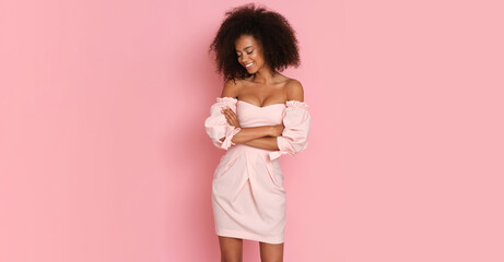 Beautiful afro american woman in a pink dress on a pink background.