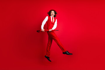 Fototapeta na wymiar Full length photo of funky guy in stylish outfit jumping and moves with parasol and dance boogie woogie isolated on red color background