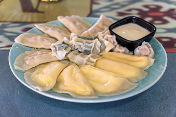 boiled dumplings with various fillings in plate with sour cream sauce on the table in a restaurant