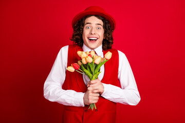 Portrait of astonished boyfriend wearing stylish vest and shirt gentleman received flowers on his birthday over red color background