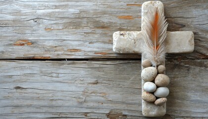 Stone cross with feather and pebbles on wood backdrop, palm sunday greetings concept