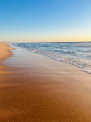 Warm colors of the seascape, sand sea coastline, sea waves on the sand, clear blue sky, no people, empty beach