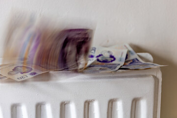 A British heating, energy cost concept with a pile of 20 pound Sterling bank notes rising from the top of a central heating radiator, giving the impression of burning, disappearing money. - obrazy, fototapety, plakaty