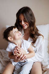 Smiling young mother hugging toddler son in pajama on bed at home