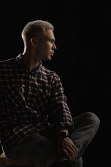 Portrait of an attractive man with blond hair in a checkered shirt on a black background.