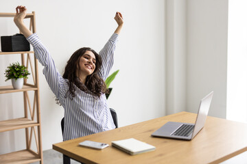 Happy excited woman at home workstation triumphing with raised hands