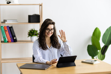 Happy business woman waving in a video conference with a tablet on a desktop