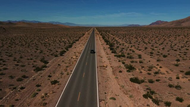 Black car driving on desert highway in Nevada. Empty street to nowhere. Road from above in the dry hot Wild West America landscape. Aerial drone