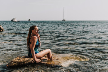 Woman beach vacation photo. A happy tourist in a blue bikini enjoying the scenic view of the sea and volcanic mountains while taking pictures to capture the memories of her travel adventure.