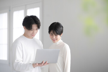 Fototapeta premium Fresh Asian (Japanese) couple looking at computers together in a bright white room Moving, house hunting and searching for rentals.