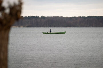 Angler standing alone on a small boat on a lake in the winter season. Fishing man in the nature and relaxing during an outdoor activity.