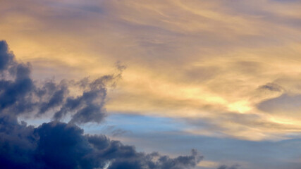 Naklejka premium Clouds at sunset. The sky is painted with bright colors by the rays of the setting sun. The rays of the setting sun pass through the clouds.