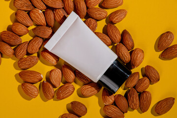 Cosmetic product in tube, bottle, lotion or serum with almonds seed on yellow background. 