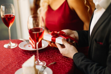 Beautiful young couple celebrating Valentine's Day in the restaurant. Exchange of gifts. Romantic day together.