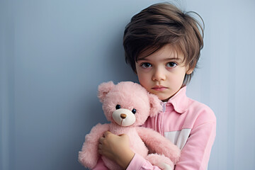 Serious boy child hugging pink teddy bear in front of blue background