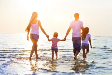 Happy young family having fun running on beach at sunset