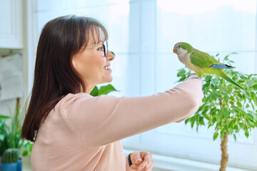 Middle aged woman bird owner holding green quaker parrot on hand