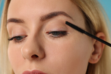 Beautiful woman applying mascara on light blue background, closeup