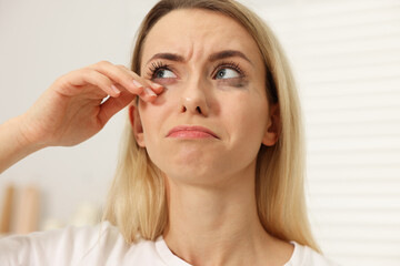 Fototapeta premium Sad woman with smeared mascara crying indoors, closeup