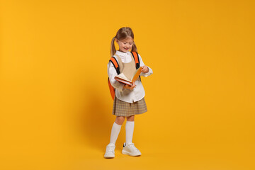 Fototapeta na wymiar Happy schoolgirl with backpack and books on orange background