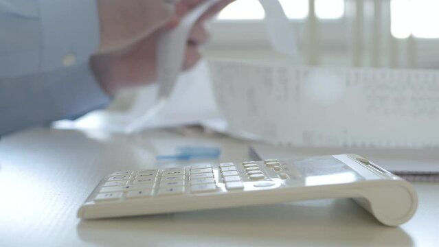 Businessman Working with Invoices, Makes Financial Calculations with Adding Machine. Accounting Fee and Taxes Calculations.