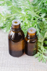Two small bottles with essential wormwood oil (extract, tincture, infusion). Old wooden background. Aromatherapy, spa and herbal medicine concept.