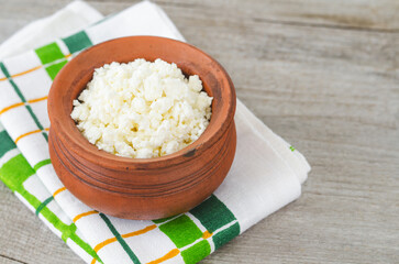 Homemade crumbly farmer's cheese in a clay pot. Wooden background. Copy space.