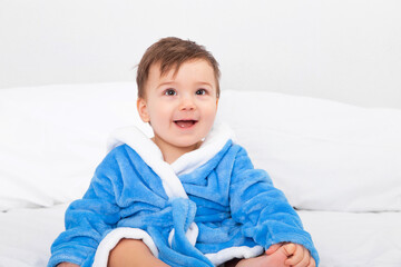 Baby in blue bathrobe, after bath, sitting on bed. Emotions, copy space.