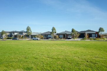 Large open space with green grass lawn with some residential houses in the background. A public park in a suburban neighbourhood with modern Australian homes. Copy space for your design.