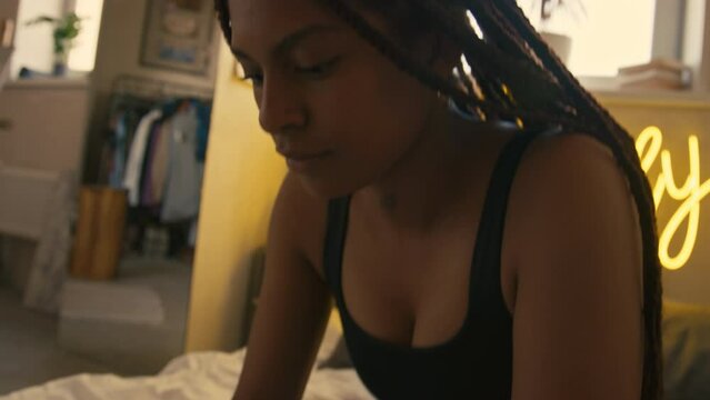 Closeup tilt lowkey slowmo of young African American freelancer typing on laptop while sitting in bed at homeCloseup tilt lowkey slowmo of young African American freelancer typing on laptop while sitt