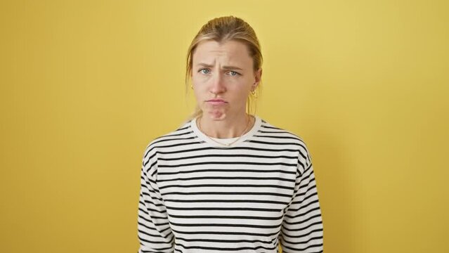 Negative nancy in a stripy tee, young blonde woman, doubtful and upset, frowns at life's problems. a grumpy portrait of failure against a sunny yellow wall.