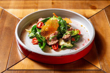 Salad of spinach leaves, tomatoes and beef. On a wooden table.