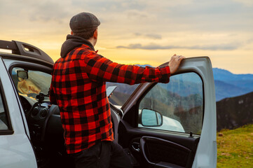 man leaning on the door of his 4x4 car with his smartphone in his hand, contemplating the mountain...