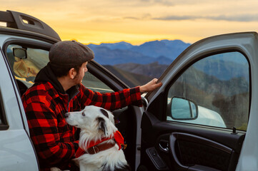 White man sitting in the seat of his 4x4 off-road car watching the sunset in the mountains with his...
