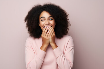 Positive beautiful African American woman with hands covering mouth laughing cheerfully against background