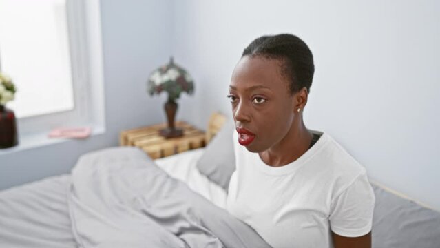Shocked african american woman lying in bed, hands on head, mouth wide open in surprise. scared, crazy expression painting the bedroom with stark fear.