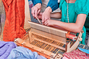 Hands of little girl weaving small rug on manual table loom and female hands of adult mentor