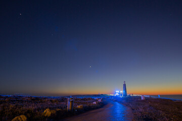 Path to the cross on a stone pillar at Cabo da Roca with fire truck with blue lights under the...