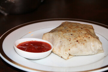 Pita bread with meat and tomato sauce on a white plate in a restaurant