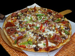Pizza with mushrooms, ham, pepper, corn, onion and cheese on a black background