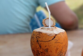 Coconut fruit drink with straw on wooden table in the park.