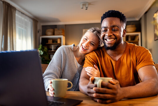 Smiling young mixed couple using a laptop while working on their home finances.