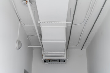 This image shows a large industrial air ventilation unit mounted on a white wall, with venting...