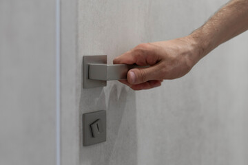 Naklejka premium A persons hand is captured as it grasps a sleek, contemporary handle, preparing to open a light grey door.