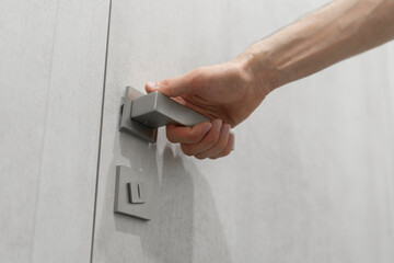 A persons hand is captured as it grasps a sleek, contemporary handle, preparing to open a light grey door.